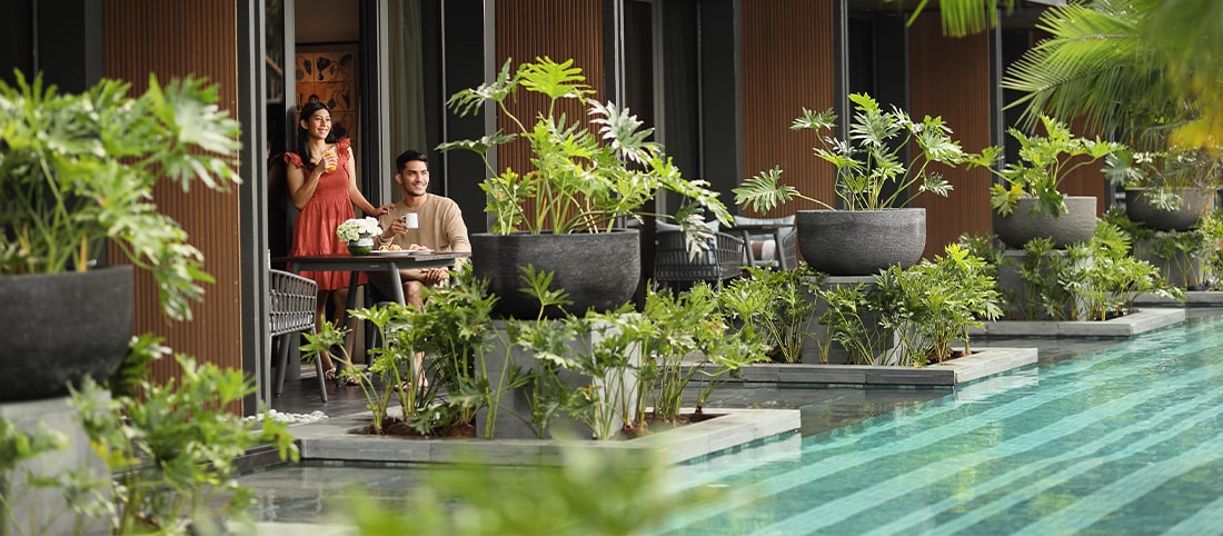 Couple sitting near pool access room, looking at the beautiful resort pool and verdant greenery in Semarang