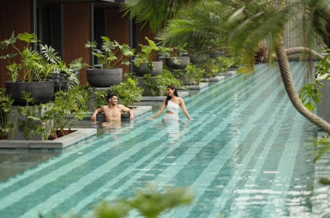 Couple smiling in a heated pool around garden in front of pool access room at Padma Hotel Semarang
